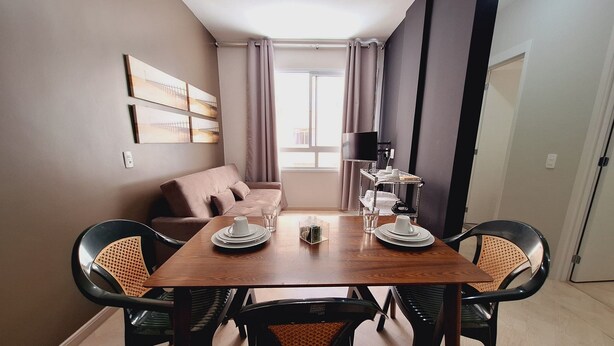A dining area with a wooden table, black chairs, a sofa, and a TV on a stand. - LK Centro 5 (Belo Horizonte)