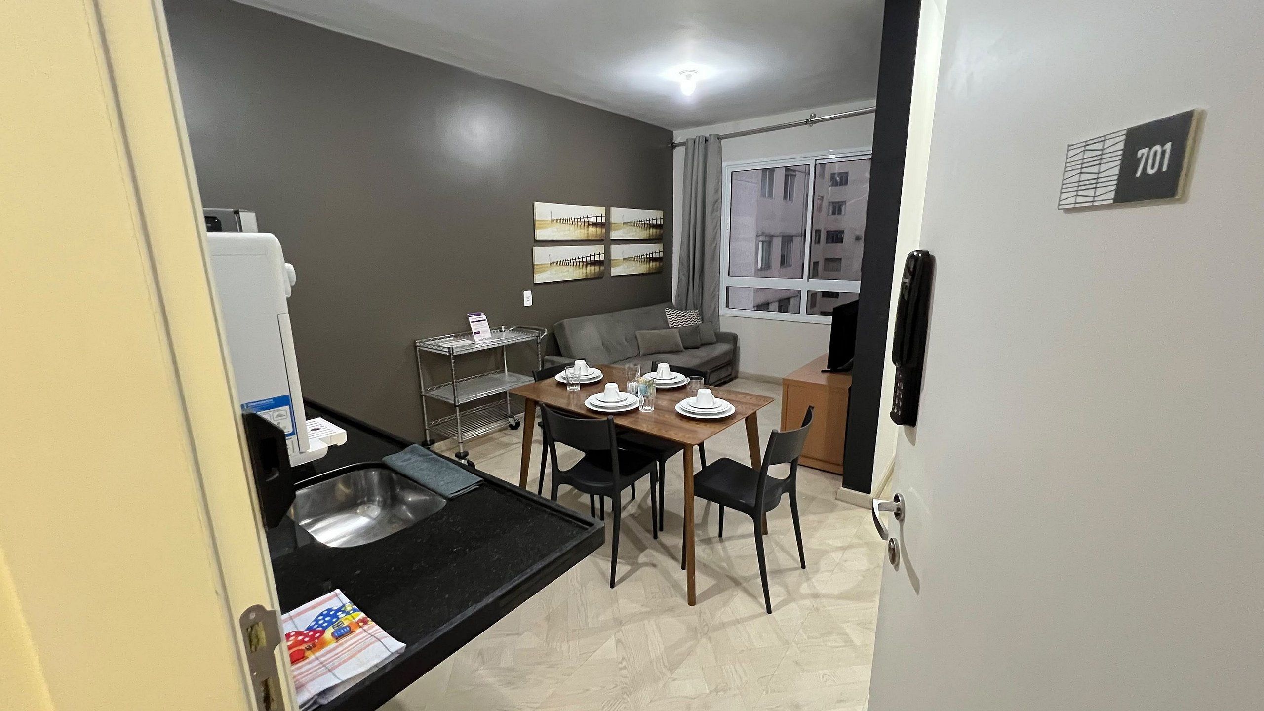 A compact kitchen with a dining table set for four, a grey sofa, and a window with curtains.