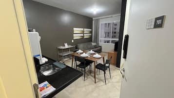 A compact kitchen with a dining table set for four, a grey sofa, and a window with curtains.