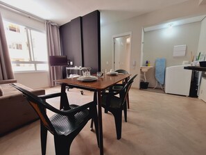 Un comedor con una mesa de madera, sillas negras, un televisor y un ventanal con cortinas.