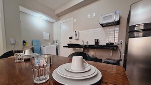 A dining table with plates and glasses, a microwave, a refrigerator, and a washing machine in a kitchen area. - LK Centro 5 (Belo Horizonte)