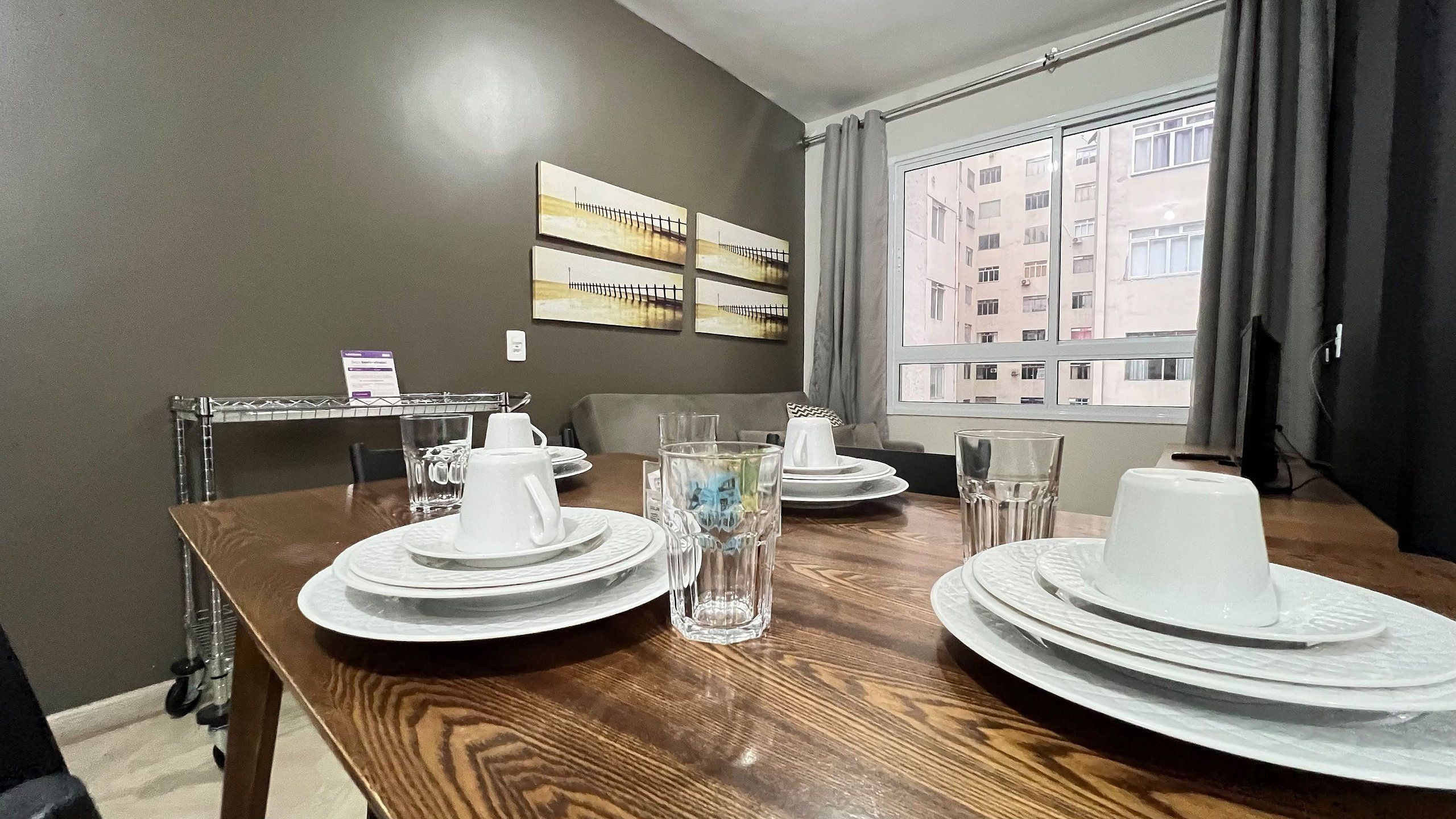 Un comedor con una mesa preparada para cuatro personas, incluyendo platos, vasos y una jarrón.