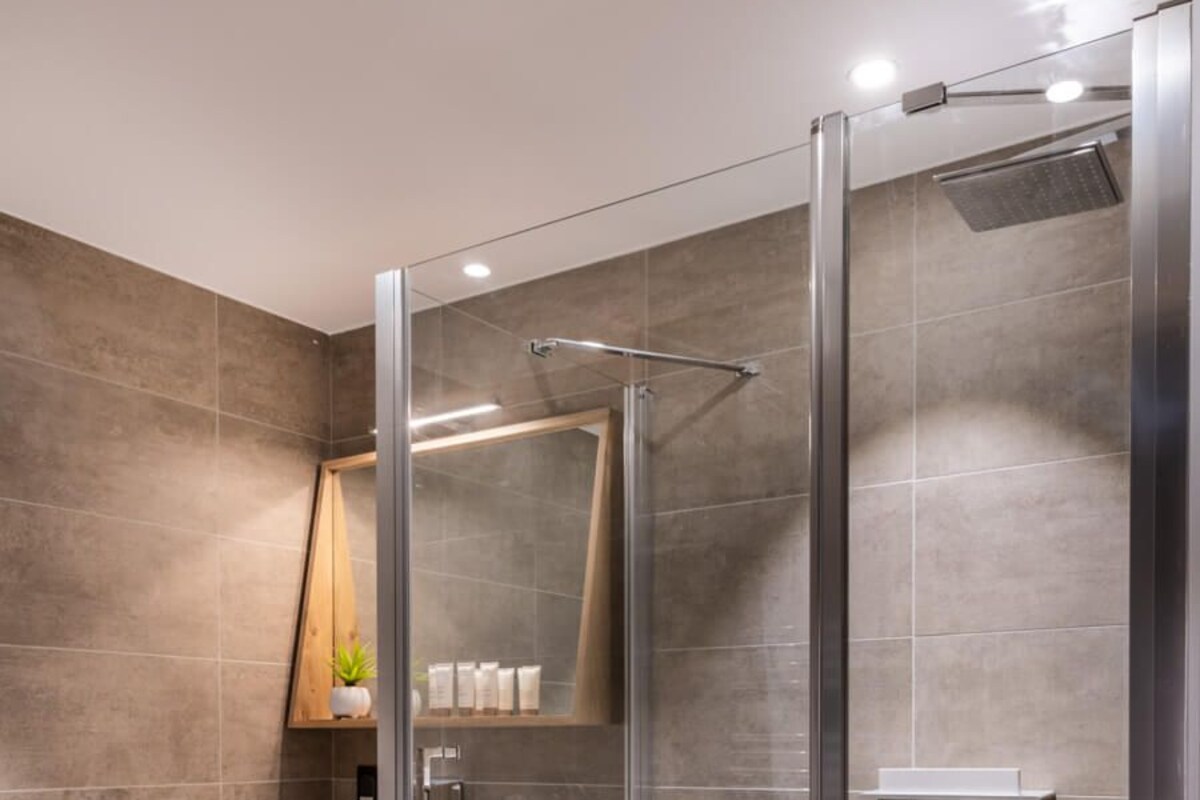 A modern bathroom with a glass-enclosed shower, a wooden vanity, and a mirror.