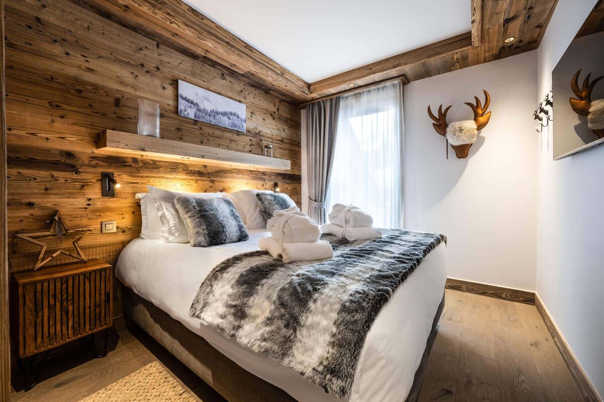 A wooden-paneled bedroom with a bed, pillows, a blanket, a star decoration, and a mounted deer head.