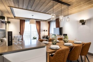 A modern dining area with a wooden table, chairs, and a television in the background. - Sundance by Alpine Resorts (Courchevel)