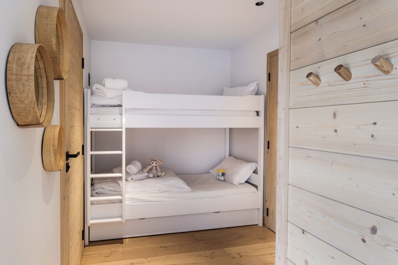 A bunk bed room with a wooden wardrobe and a shelf with folded towels.