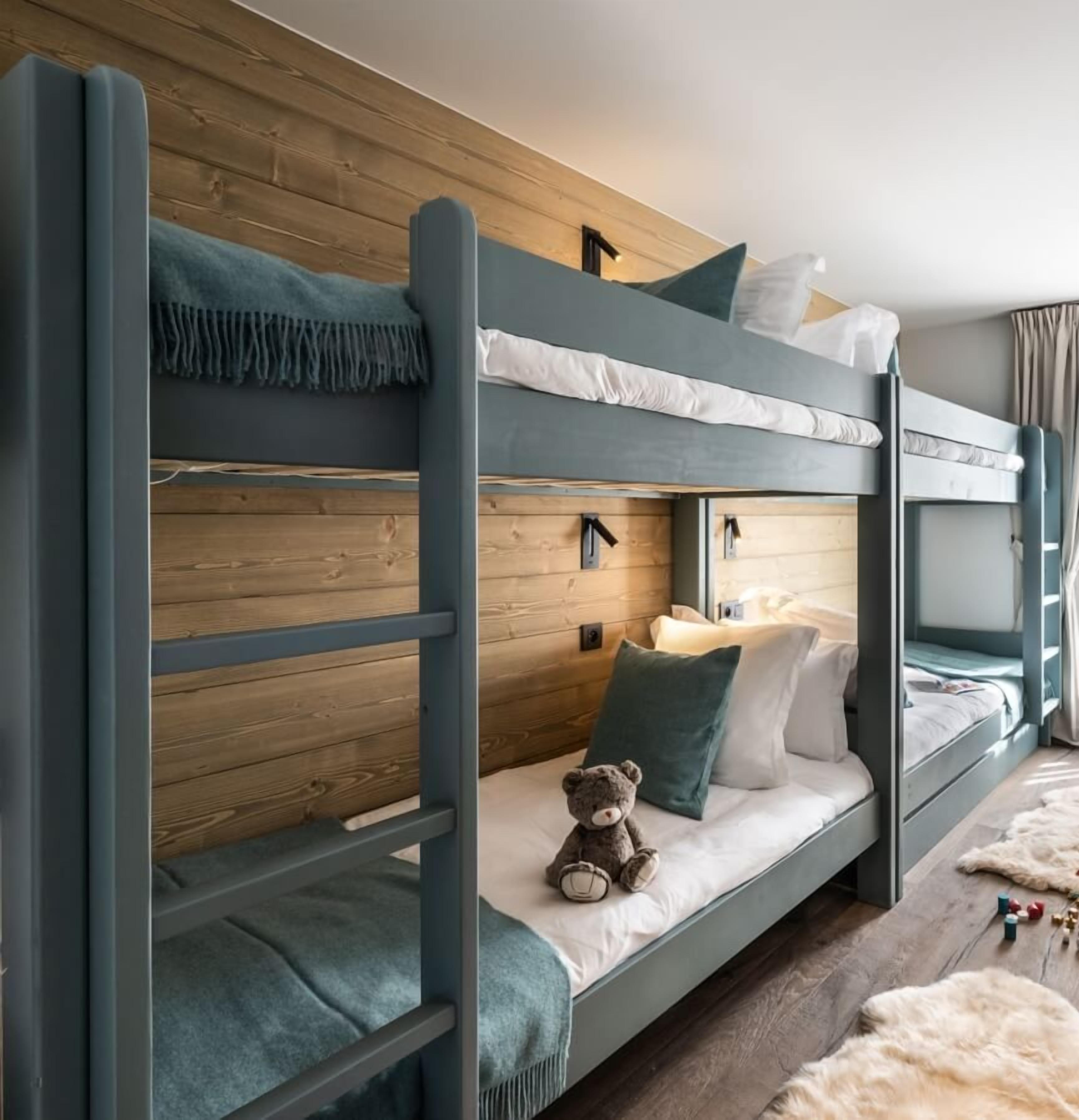 A bunk bed room with a wooden headboard, a teddy bear on the lower bunk, and a window with curtains.