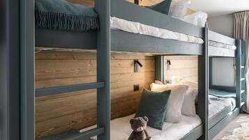 Habitación con literas de madera, un osito de peluche en la cama inferior y una ventana con cortinas.