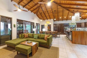 A spacious living area with a large green sofa, wooden coffee table, and a dining area with a wooden table and chairs. - Ocean View 5BR Chontales Villa w/ Pool, Sleeps 12 (Puntarenas)