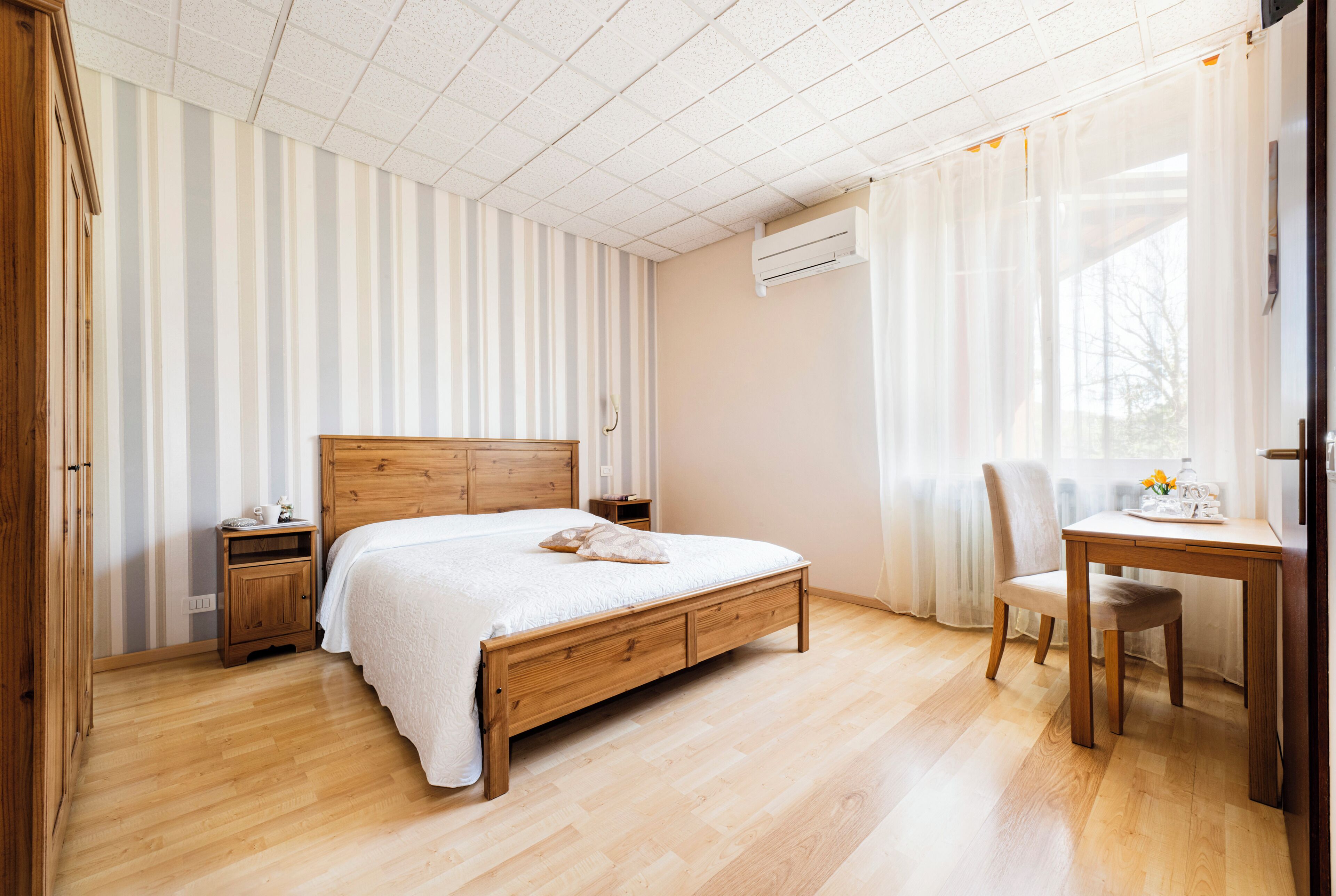 Un dormitorio con una cama de madera, una mesita de noche, una silla, una mesa y una ventana con cortinas.
