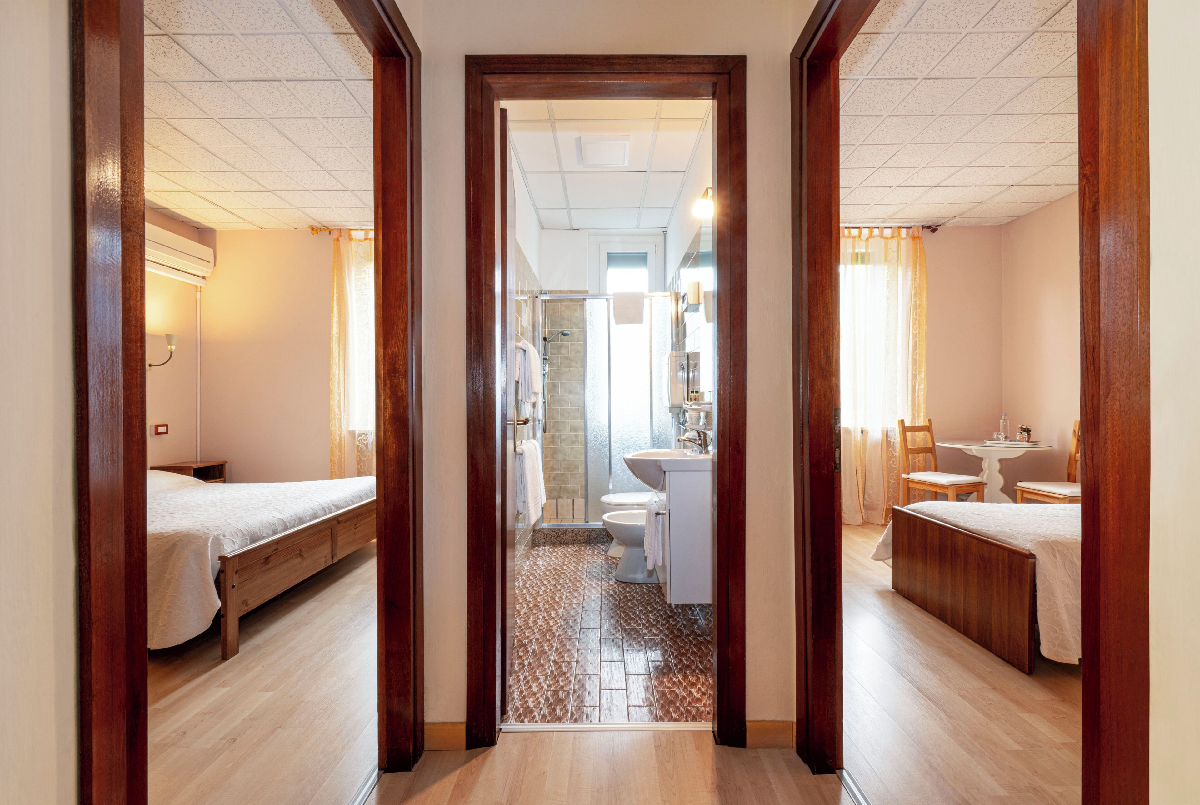 A hallway leading to a bathroom with a shower, toilet, and sink. There are two beds on either side of the hallway.
