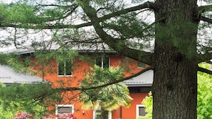 A building with a red facade, surrounded by lush greenery and flowering bushes. - Villa Ferrari Hotel Garni (San Maurizio d'Opaglio)