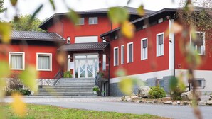 A red and white building with a staircase leading to the entrance, a small garden area, and a paved driveway. - Villa Ferrari Hotel Garni (San Maurizio d'Opaglio)