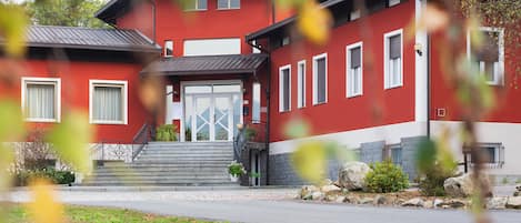 Punavalkoinen rakennus, jossa on portaikko, joka johtaa sisäänkäynnille, pieni puutarha-alue ja asfaltoitu ajotie.