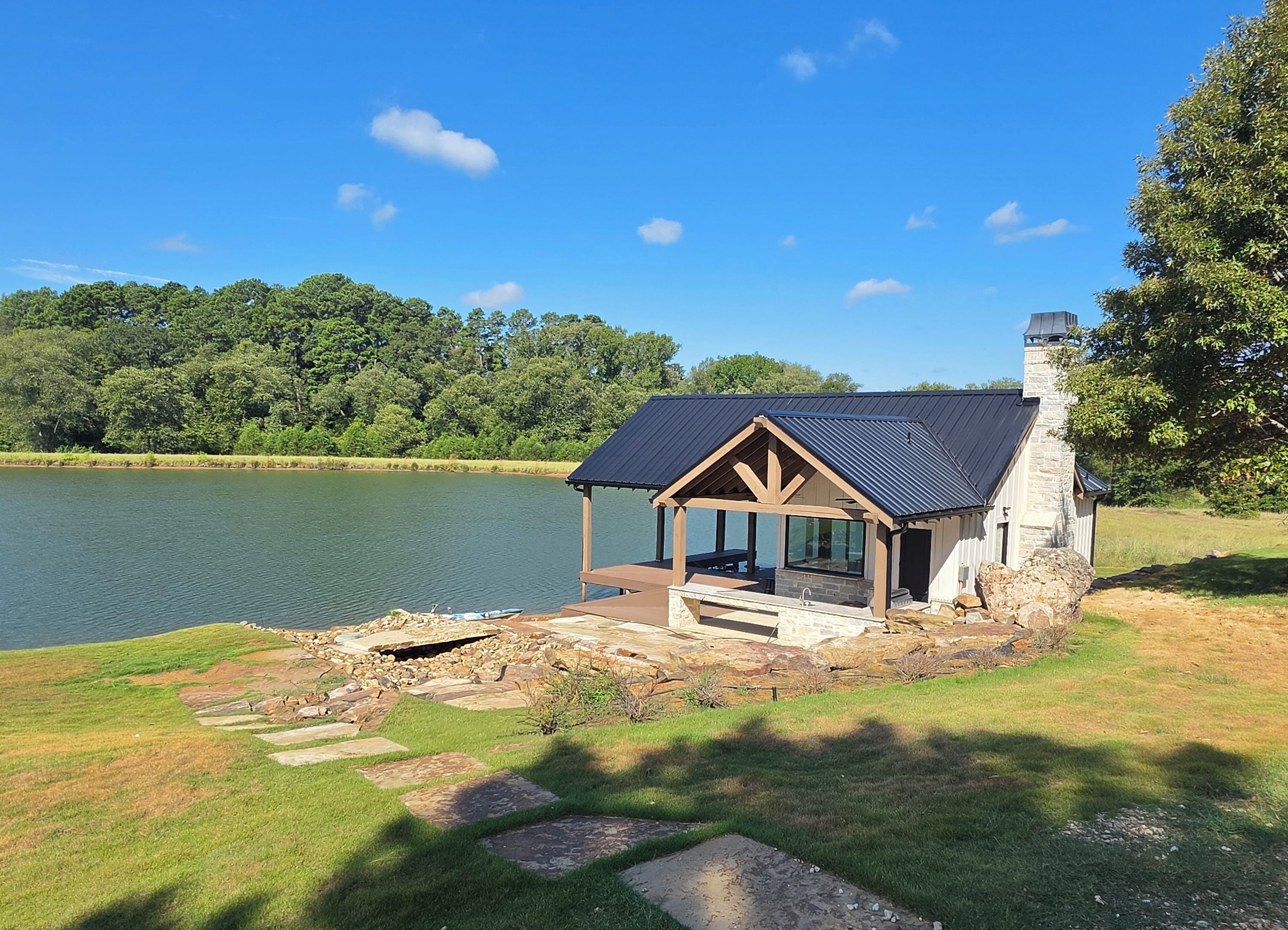 A lakeside cabin with a covered patio, stone steps, and a stone chimney.