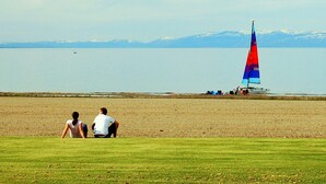 A beach with a sailboat in the distance, a grassy area in the foreground, and mountains in the background. - `The Alice` in Ideal Beach Resort (Garden City)