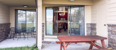 A patio with a wooden table and chairs, a glass door leading to an interior space, and a stone wall on one side.
