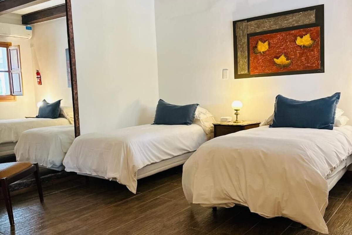 A hotel room with two beds, a wooden floor, a mirror, and a framed artwork on the wall.