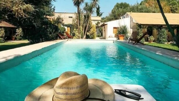 A swimming pool with a hat and sunglasses on the edge, surrounded by palm trees and a clear sky. - Casa de Coria (Chacras de Coria)
