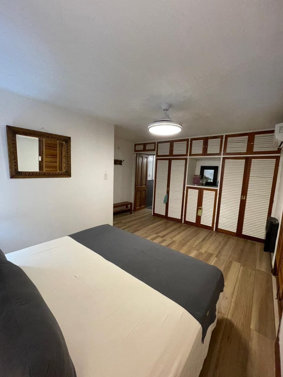 Ein Zimmer mit einem Bett, einem Kleiderschrank, einem Spiegel und einem Deckenventilator.