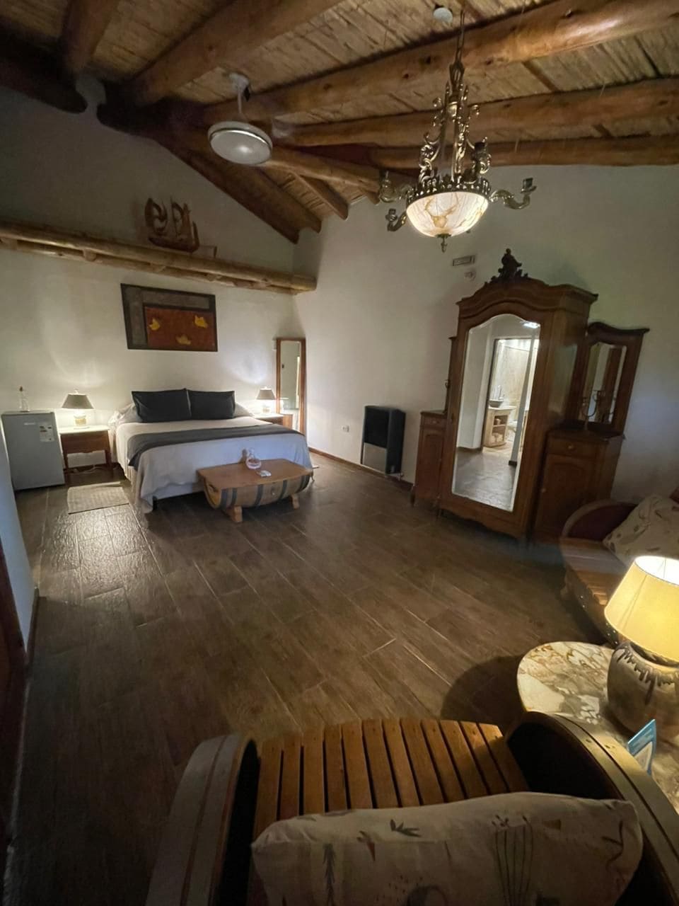 Quarto com cama, piso de madeira, lustre, espelho e uma pequena mesa.