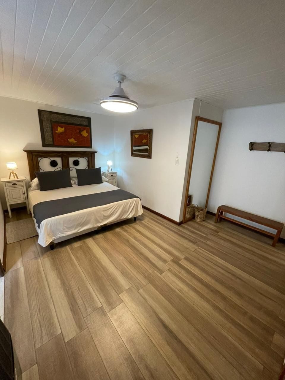 A bedroom with a bed, bedside tables, a ceiling fan, and a wooden floor.