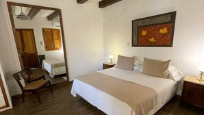 A bedroom with a large bed, wooden beams, a ceiling light, a painting, and a chair. - Casa de Coria (Chacras de Coria)