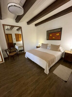 A bedroom with a large bed, wooden beams, a ceiling light, a painting, and a chair. - Casa de Coria (Chacras de Coria)