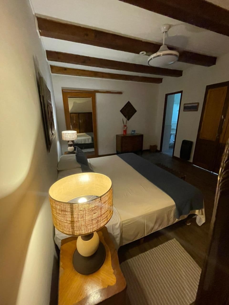 A bedroom with a bed, a bedside lamp, a dresser, a mirror, and a ceiling fan.