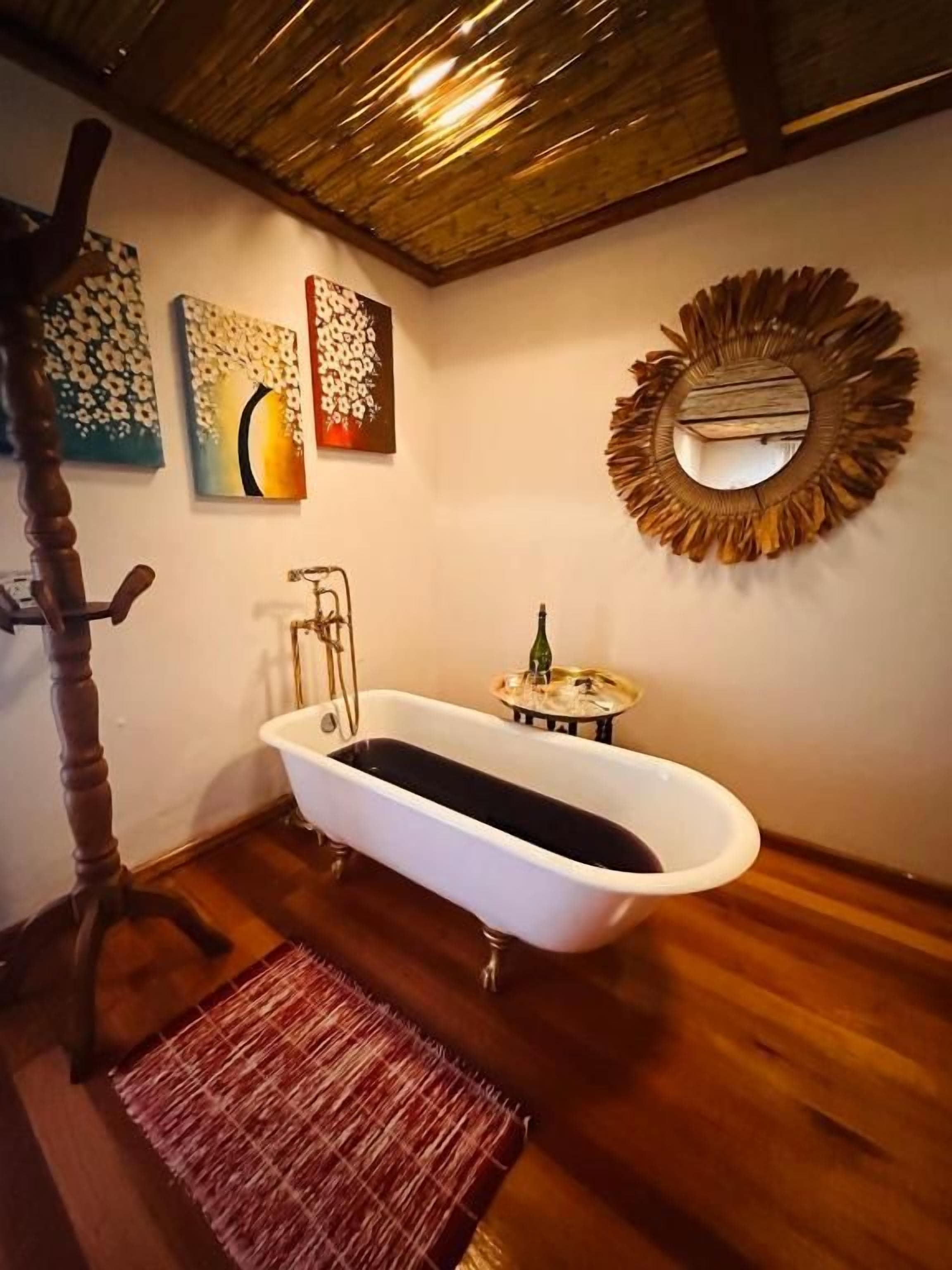 Une salle de bain avec une baignoire sur pieds, un plancher en bois, un miroir doté d’un cadre décoratif et des œuvres d’art accrochées au mur.