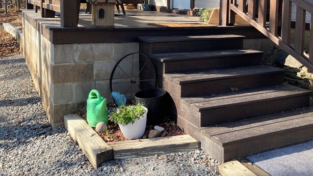 A covered porch with steps leading to a door, a wheelbarrow, and potted plants. - Sweetdillatpicklesgap (Conway)