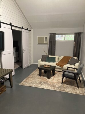 A living room with a white sofa, a coffee table, a dark armchair, a sliding door, and a window with curtains. - Sweetdillatpicklesgap (Conway)