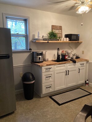 A kitchen with a refrigerator, microwave, coffee maker, and a window with a view of trees. - Sweetdillatpicklesgap (Conway)