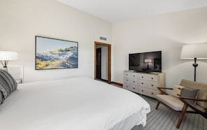 Ein Hotelzimmer mit einem großen Bett, einem Fernseher, einem Schminktisch, einem Stuhl und einem Gemälde an der Wand.