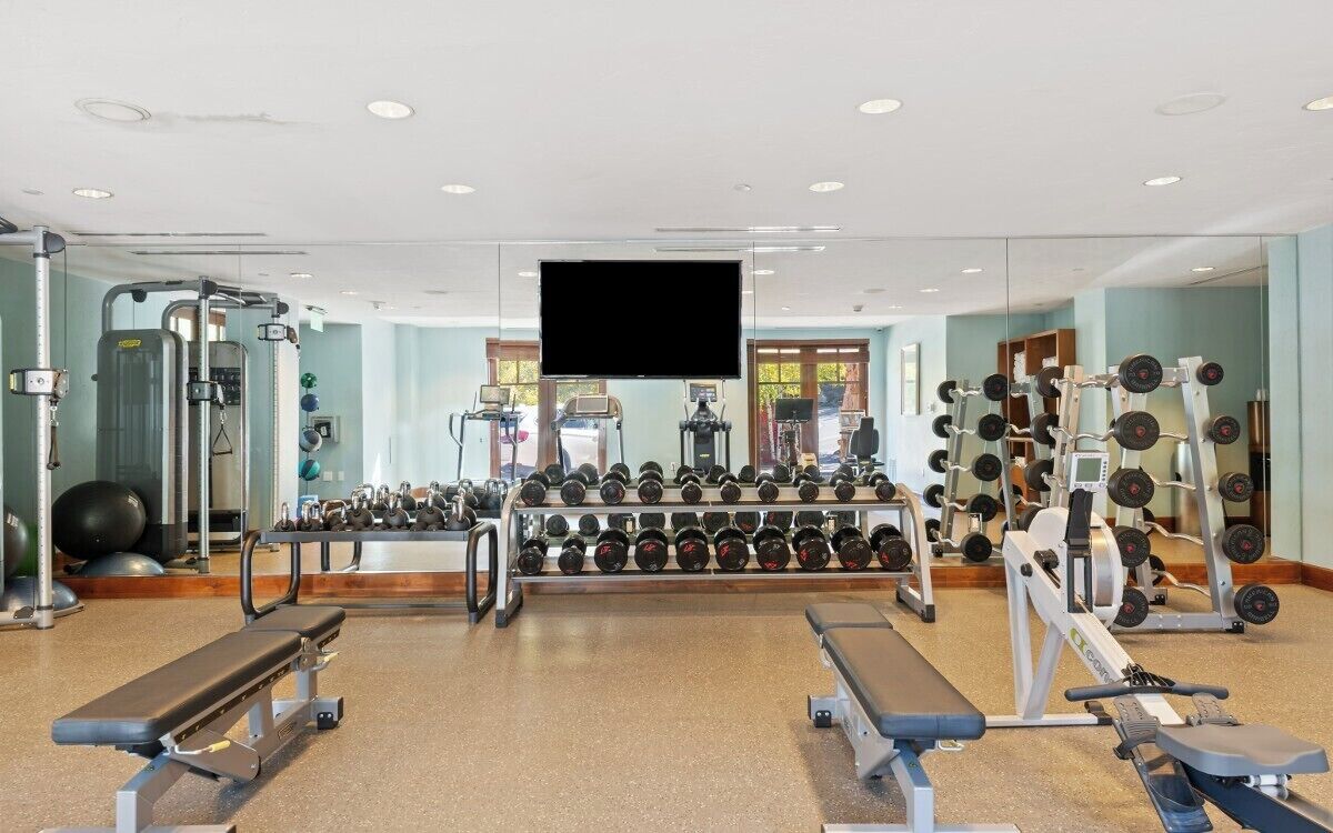 Een sportschool met gewichthefapparatuur, loopbanden en een televisiescherm.