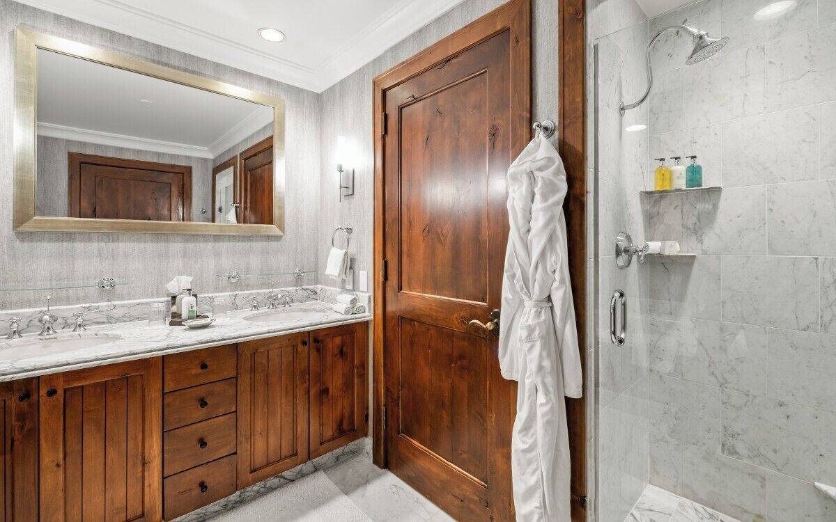 A bathroom with a wooden vanity, a large mirror, a shower with a handheld showerhead, and a towel rack.