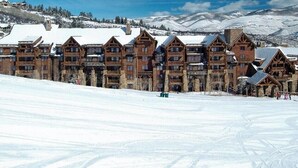 A large lodge with multiple wooden buildings, a ski slope in the foreground, and snow-covered mountains in the background. - 3BR SKI-IN/OUT JAN 2-9, FREE LIFT TICKETS -FORMALLY TIMBERS/RITZ BACHELOR GULCH (Avon)
