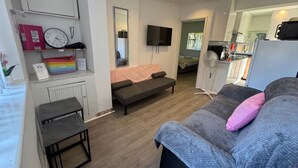 Ein modernes Wohnzimmer mit einer Couch, einem kleinen Tisch, einem Fernseher und einer Küchenzeile im Hintergrund.