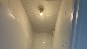 Ein kleines, schmales Badezimmer mit weißen Fliesen, einer Toilette, einem Waschbecken und einer Deckenleuchte.