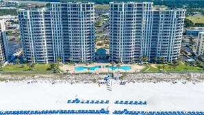 A high-rise hotel with multiple floors, a central pool, and a beach area with umbrellas. - Silver Beach Towers 102w- Southern Heirs (Destin)