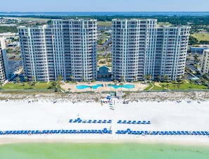 A high-rise hotel with multiple floors, a central pool, and a beach area with umbrellas. - Silver Beach Towers 102w- Southern Heirs (Destin)