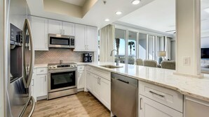 A modern kitchen with stainless steel appliances, white cabinetry, and a large window overlooking a balcony. - Silver Beach Towers 102w- Southern Heirs (Destin)