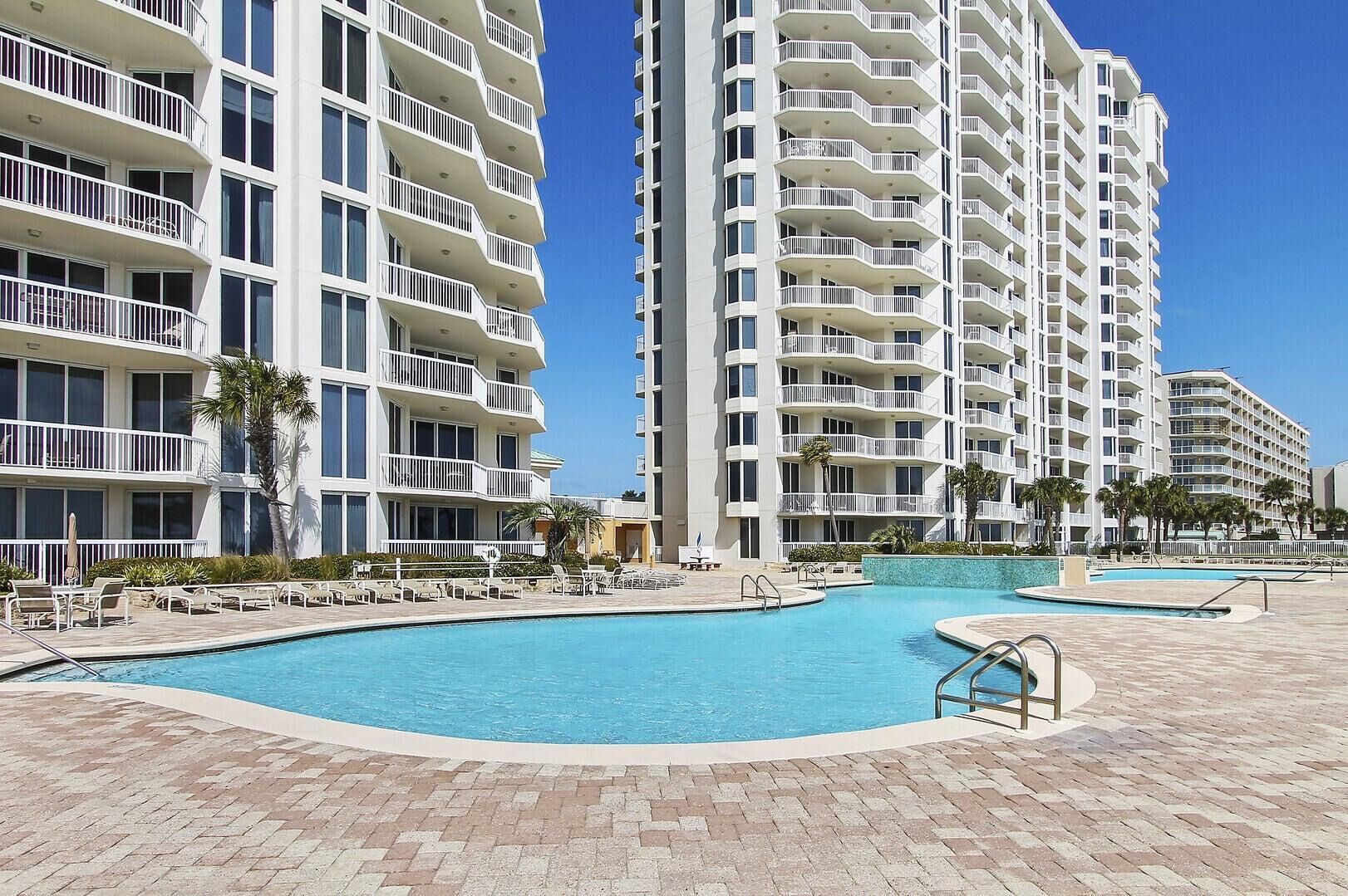 A hotel with multiple balconies, a swimming pool, and palm trees.