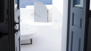 An open door leading to a balcony with a white table and two glasses, overlooking a body of water and distant land. - Eros suites Oia (Oia)