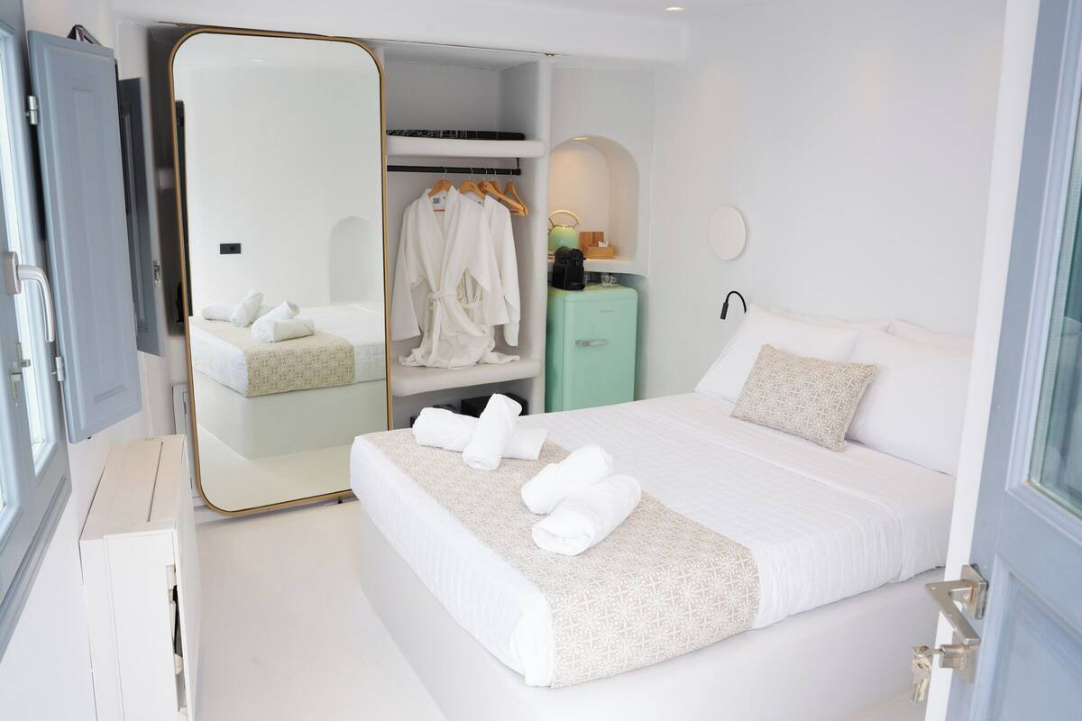 A modern hotel room with a large bed, a walk-in closet, a small seating area, and a mirror.