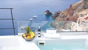 A balcony with a view of the sea, a hot tub, and a fruit bowl with bananas and oranges. - Eros suites Oia (Oia)