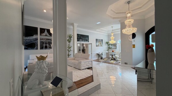 A spacious living area with a white sofa, a glass coffee table, and a chandelier.