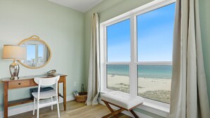 Una habitación con escritorio, silla y un ventanal con vista a la playa.
