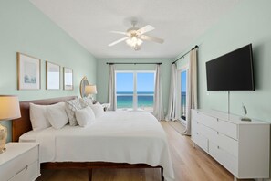 Ein Schlafzimmer mit Bett, Deckenventilator, Fernseher, Fenster mit Meerblick und einem Schminktisch.