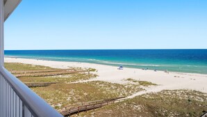 Vista de la playa con un paseo marítimo de madera, cielo azul despejado y mar tranquilo.